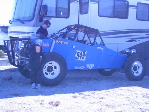 1990 Ford Bronco - blue tube-frame off-road buggy marked 949 parked beside a motorhome, with a small child and a person standing by it.