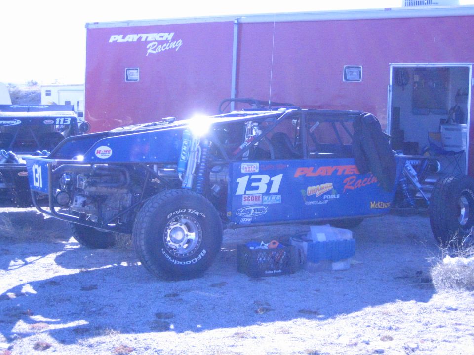 Blue off-road race buggy number 131 in front of Playtech Racing trailer