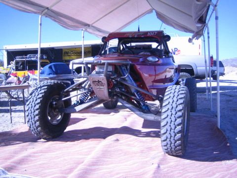 1990 Ford Bronco - dark red tube-frame off-road race buggy marked 1017 sits on large knobby tires under a shade canopy at a desert event.