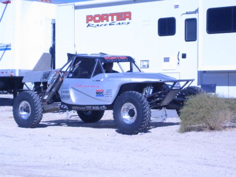 1990 Ford Bronco - silver tube-frame off-road race buggy marked 1040 parked in front of a white trailer lettered Porter Race Cars.
