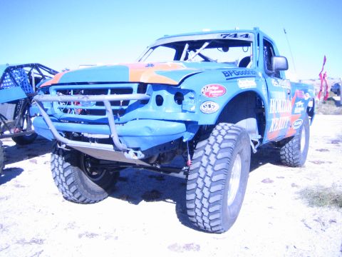 1990 Ford Bronco - blue and orange off-road race truck numbered 744 with Horizon Realty graphics shows front-end damage in the desert.