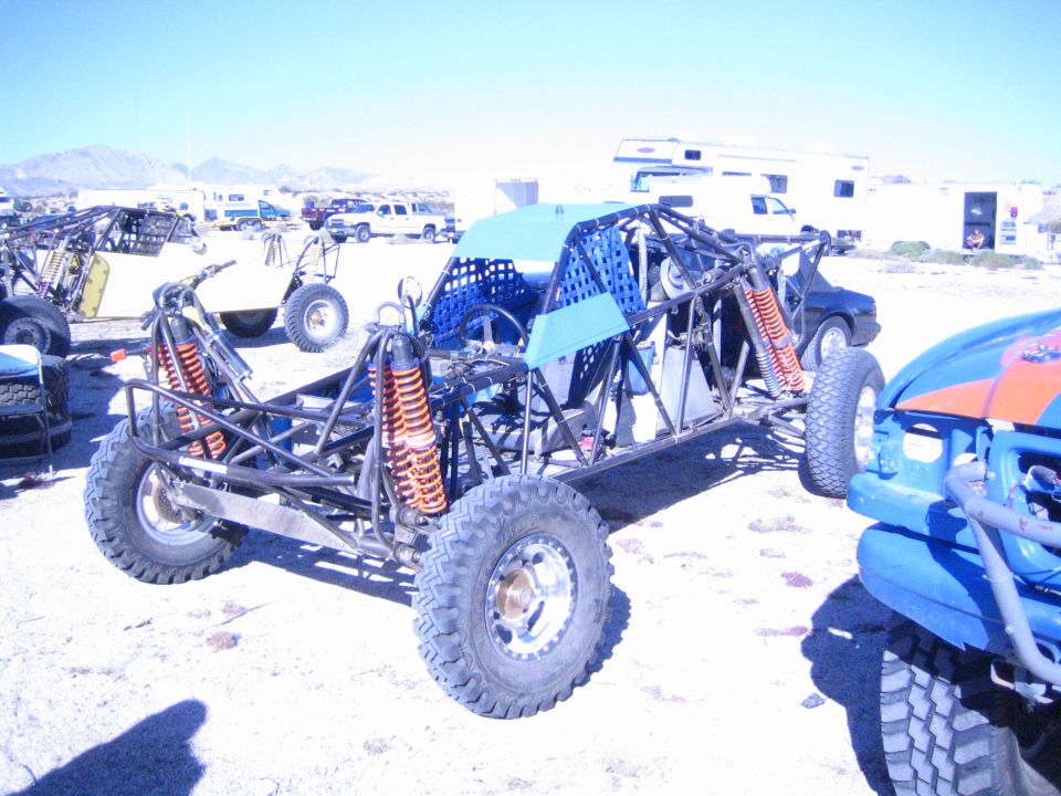 Bare tube-frame off-road race buggy chassis parked in a desert pit
