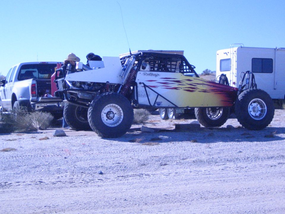White off-road race buggy with flame graphics parked by a pickup and RV