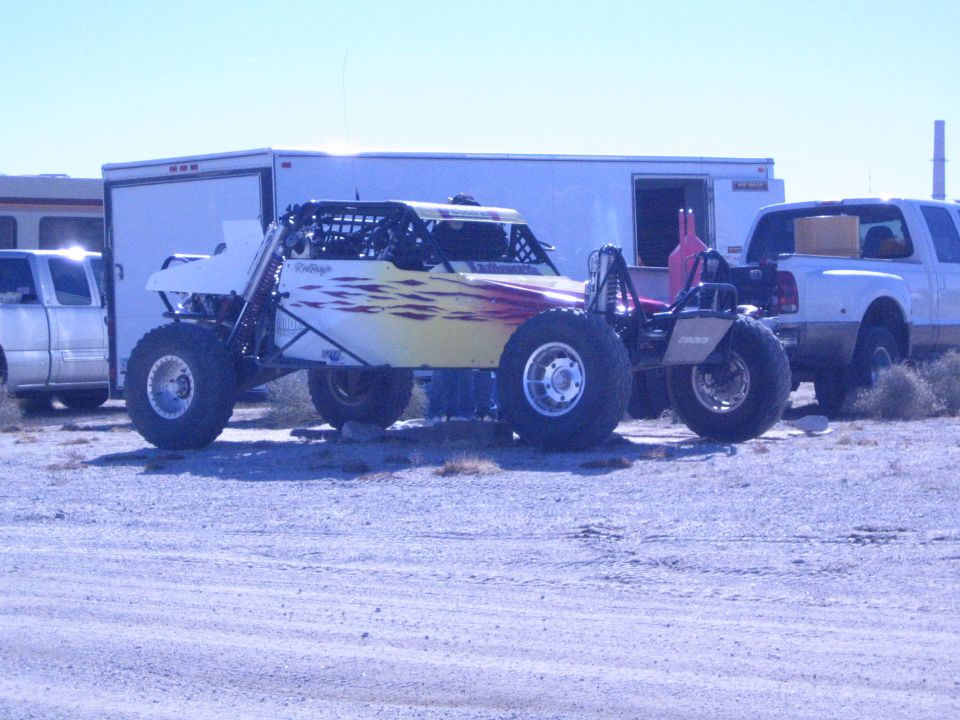 White off-road buggy with flame graphics between a trailer and pickups