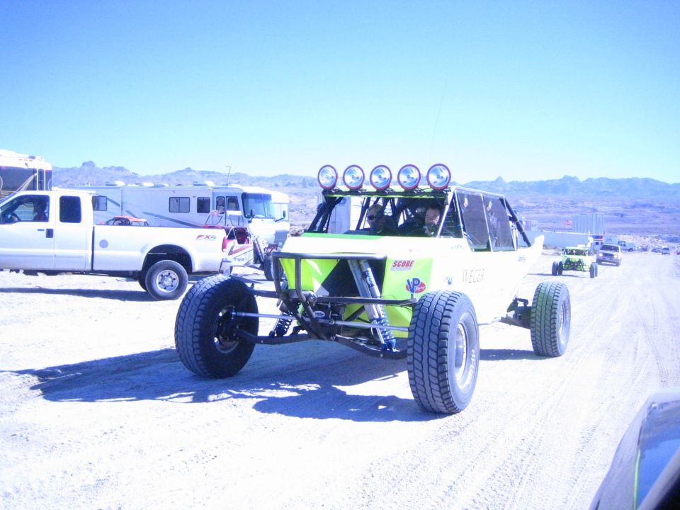 Green and black off-road race buggy with five roof lights on a desert road