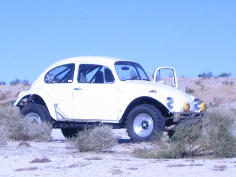1990 Ford Bronco - cream-colored Volkswagen Beetle converted into a Baja bug, with roll cage and off-road tires, sits in open desert.