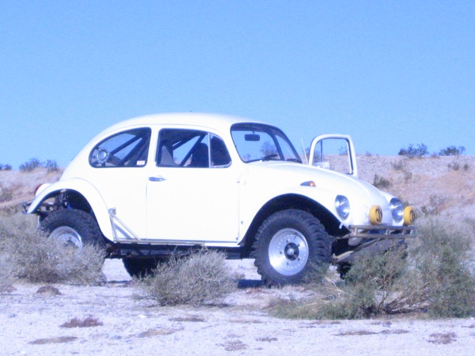 Cream-colored Volkswagen Beetle Baja bug with roll cage and knobby tires on desert terrain