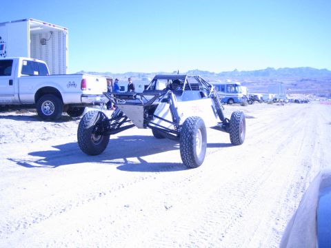 1990 Ford Bronco - white single-seat tube-chassis off-road buggy sits on a desert dirt road near a white pickup truck and enclosed trailer.