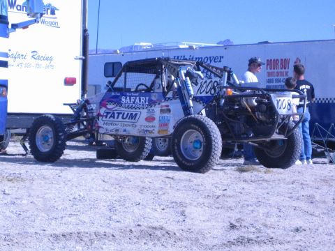 1990 Ford Bronco - sponsored off-road race buggy marked 1008 with Tatum Motorsports and Safari Offroad decals sits in a pit as crew stand nearby.