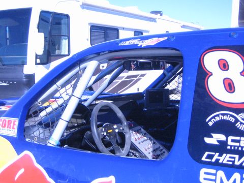 1990 Ford Bronco - cockpit of a blue race truck numbered 8 shows the roll cage, steering wheel and window net, with an RV parked behind.