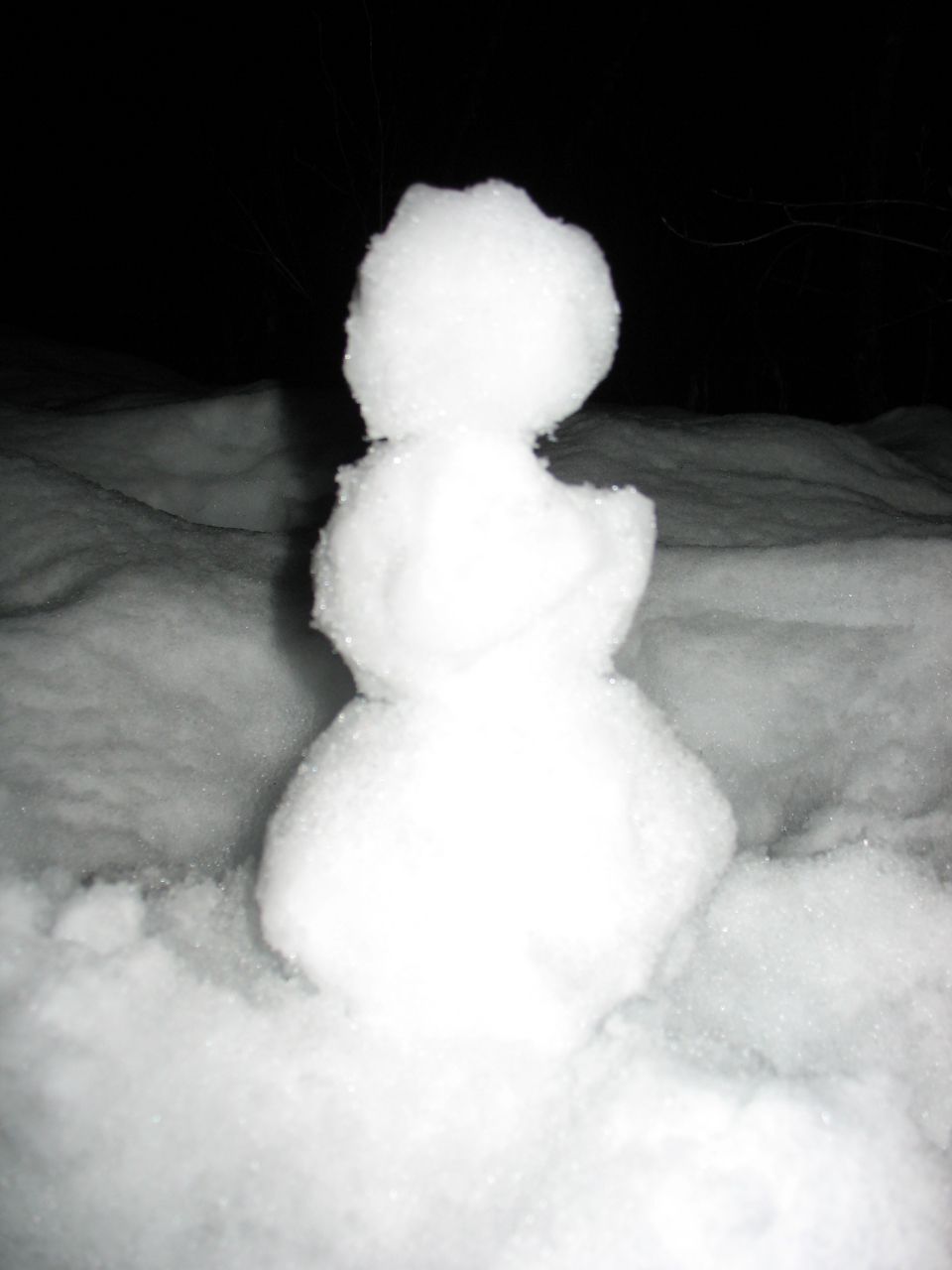 Small three-ball snowman built on snow at night against dark background