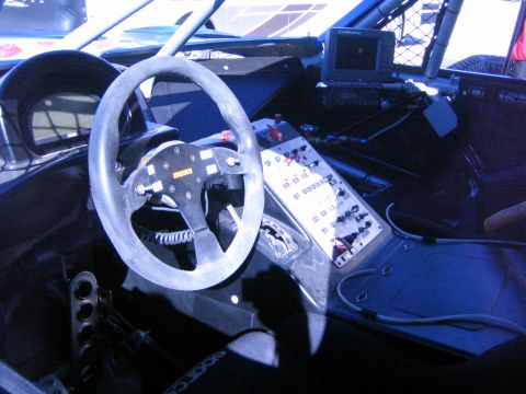 1990 Ford Bronco - interior of an off-road race vehicle showing a suede-rimmed steering wheel, aluminum switch panel and a dash-mounted GPS screen.