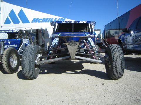 1990 Ford Bronco - front of a blue McMillin-marked tube-chassis off-road buggy number 100 sits on dirt under a tent beside another race buggy.