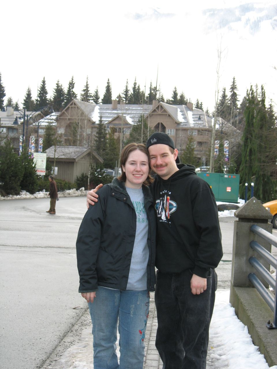 Couple posing in front of lodge-style buildings with snow on the ground