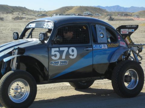 1990 Ford Bronco - black and blue Volkswagen Beetle-bodied off-road race car numbered 579 with a driver inside is driven across open desert terrain.