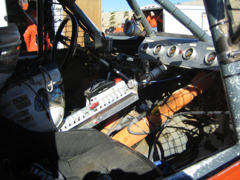 1990 Ford Bronco - Bare interior of a race truck showing a roll cage, gauge cluster and orange fuel cell area.
