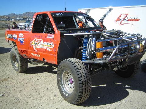 1990 Ford Bronco - orange AZ Land Racing off-road truck numbered 800 with blue coilover shocks and tube bodywork parked in a desert pit.
