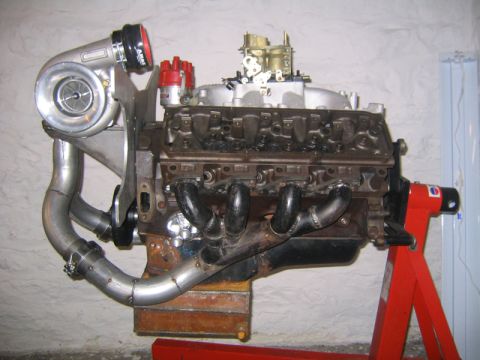 1969 Ford Mustang - A V8 engine with a turbocharger and custom exhaust components is displayed on a stand.