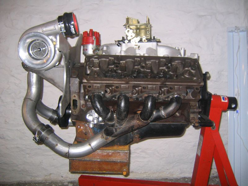 Turbocharged V8 engine on a red stand, with custom exhaust manifold and carburetor