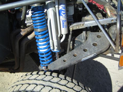 1990 Ford Bronco - Close-up of a blue-coil Fox shock and fabricated suspension components on an off-road race truck above a large tire.