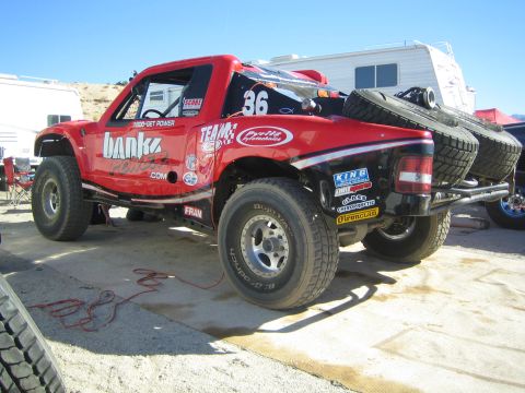 1990 Ford Bronco - red off-road race truck numbered 36 with Banks Power branding sits in a pit carrying two spare tires on its rear rack.
