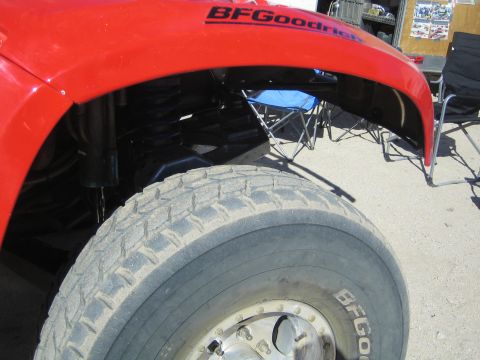1990 Ford Bronco - Close-up of a red fender with a BFGoodrich decal above a large BFGoodrich off-road tire and folding chairs behind.