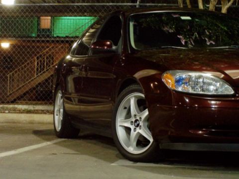 1999 Ford Taurus - The front passenger side of a sedan is visible, parked in a lot at night.