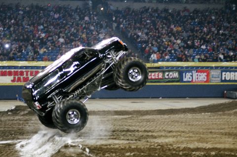 1976 Ford F-150 - A monster truck performs a jump during a Monster Jam event, kicking up dirt.
