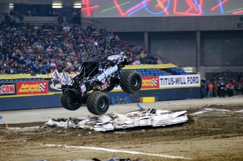 1976 Ford F-150 - A monster truck soars through the air over a pile of crushed cars during an event at an arena.