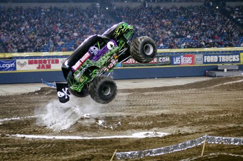 1976 Ford F-150 - Monster truck performing a jump at an indoor event with "Monster Jam" signage visible.