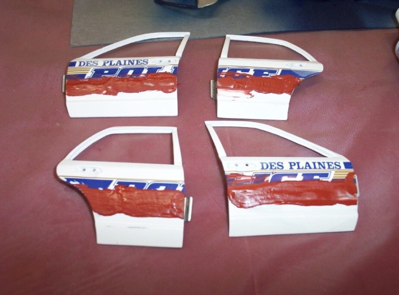 Four white car doors with red paint and 'DES PLAINES POLICE' text