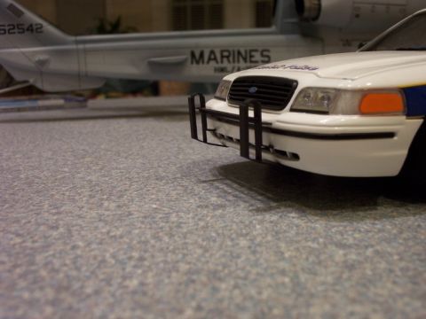 1998 Ford Crown Victoria - A model police car is parked in front of a model of a Marines aircraft.