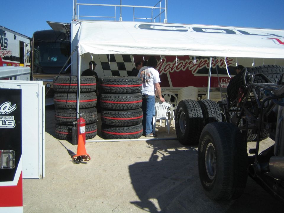Stacks of off-road race tires under a Collins Motorsports canopy