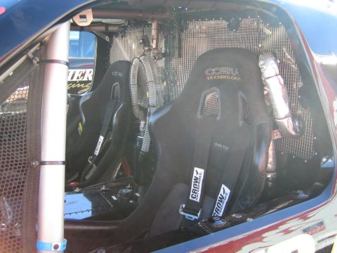1990 Ford Bronco - Pair of black Cobra Technology racing bucket seats with harnesses inside a roll-caged off-road truck cab beside a heat-shielded exhaust.