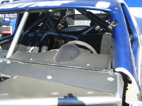 1990 Ford Bronco - View into the stripped interior of a blue off-road race truck showing the roll cage, switch panels and a black composite firewall.