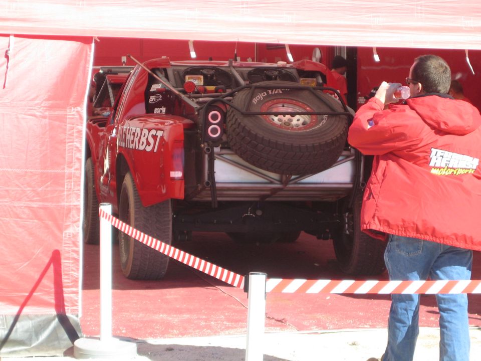 Rear of red Terrible Herbst race truck with spare tire under a canopy