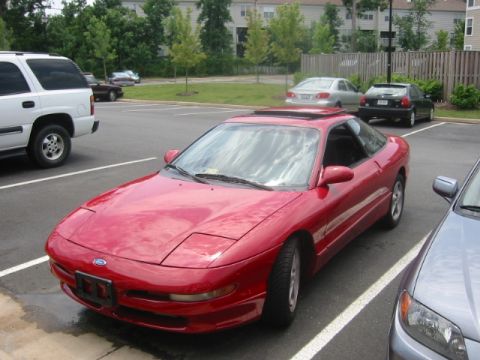 1993 Ford Probe - A red 1993 Ford Probe is parked in a lot next to other vehicles.