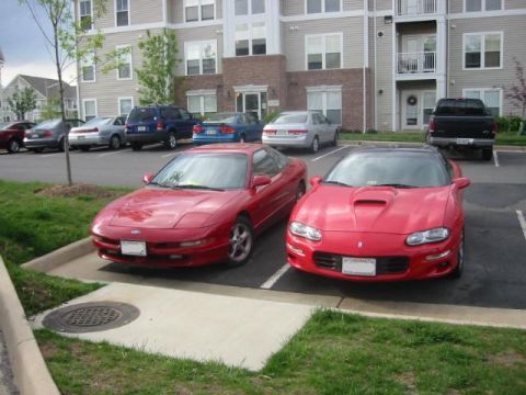 1993 Ford Probe - Two red sports cars, a 1993 Ford Probe and a Chevrolet Camaro, are parked side-by-side in a lot.