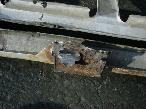 1966 Ford F-250 - This close-up shows a heavily rusted metal bracket with a circular hole, likely part of a vehicle's undercarriage.