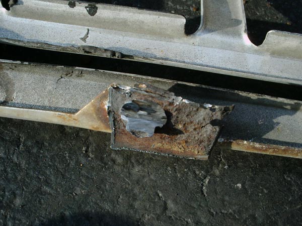 Torn-open rusty mounting tab ground to bare metal on a truck grille panel