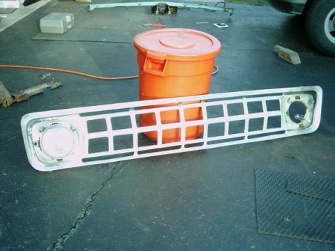 1966 Ford F-250 - A white grille with square openings and a headlight cutout, likely from a 1966 Ford F-250, rests on a dark surface.