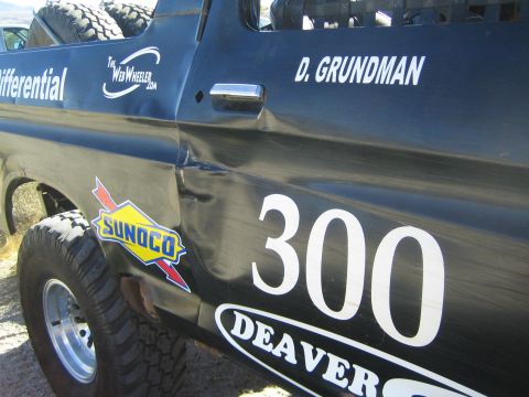 1990 Ford Bronco - Side body detail of a black race truck showing the #300, driver name D. Grundman, a Sunoco decal and creased fender damage.
