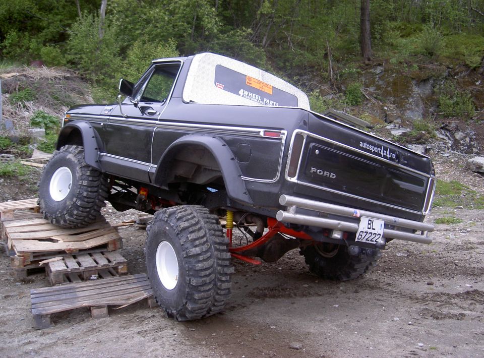 Modified black Ford Bronco with oversized tires, lifted suspension, and custom rear bumper, positioned on wooden pallets