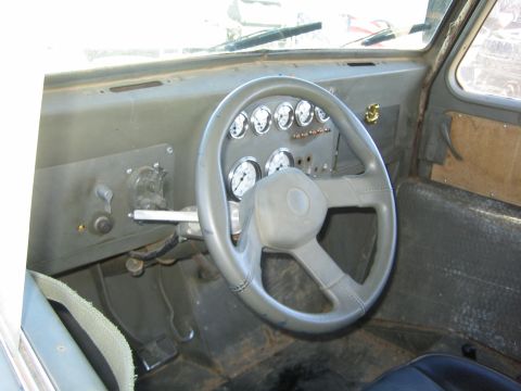 1990 Ford Bronco - worn interior of an older vehicle shows a flat gray dashboard with a cluster of round gauges and a gray steering wheel.