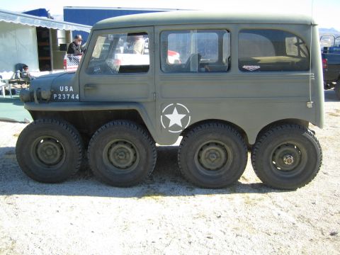 1990 Ford Bronco - Side profile of an olive-drab eight-wheeled military-style wagon marked USA P23744 with a white star, parked on dirt.