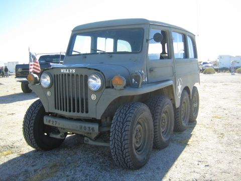 1990 Ford Bronco - olive-drab eight-wheeled Willys-badged vehicle with round headlights and a white star sits on a dirt lot near a flag.