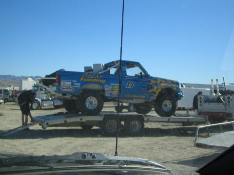 1990 Ford Bronco - Seen through a windshield, a blue Ford race truck #973 with Goodyear and Solar Funding decals is loaded on a flatbed trailer.