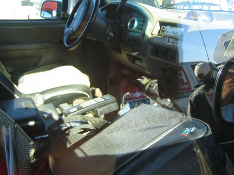 1990 Ford Bronco - dusty interior of a Ford cab shows the steering wheel, dashboard, aftermarket stereo and handheld radios on the seat.