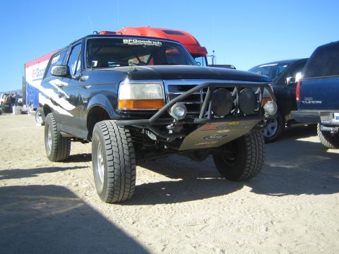 1990 Ford Bronco - lifted black Ford Bronco with a tubular offroad bumper and round light pods sits in a sandy desert pit area.