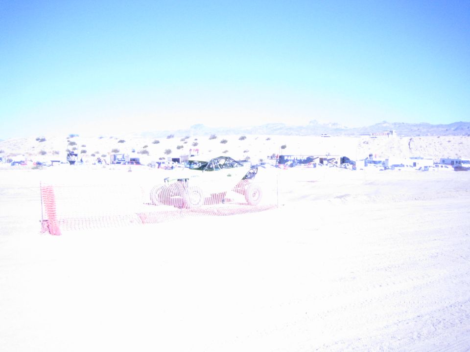 Offroad race car behind orange safety fencing on a bright desert course